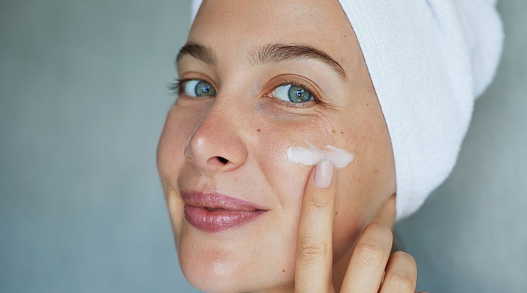 mulher branca aplicando creme facial na face